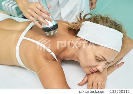 Caucasian female receiving back massage with special device in spa setting 133250311