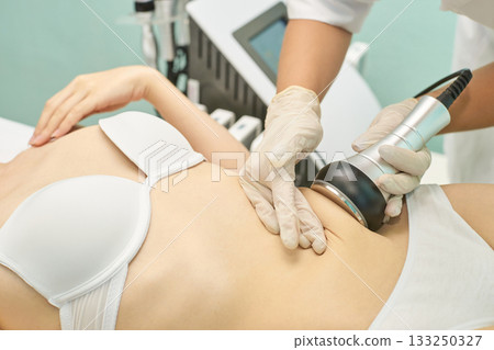 Asian female undergoing cavitation treatment for body contouring at spa clinic Asian female undergoing cavitation treatment for body contouring at spa clinic 133250327