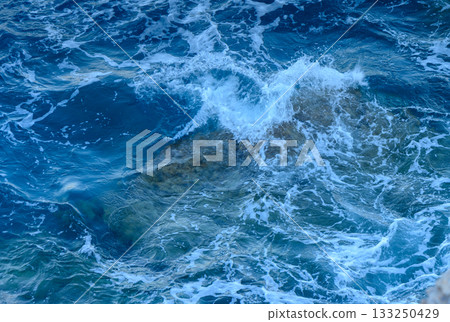 Waves crashing over sunlit rocks in the turquoise waters of a serene coastal destination. 133250429