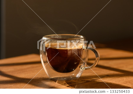A steaming cup of coffee rests on a wooden table bathed in warm sunlight A steaming cup of coffee rests on a wooden table bathed in warm sunlight 133250433
