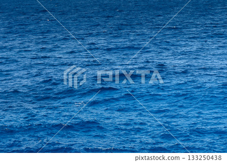 Vibrant blue ocean waves gently dance under the sunlight by the tranquil shore. 133250438