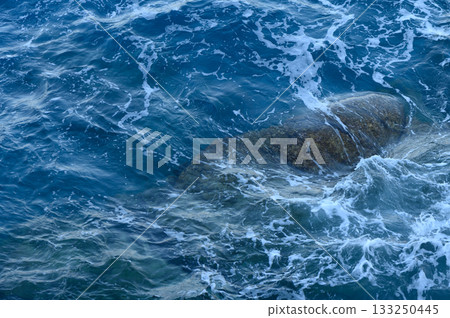 Gentle waves lap against rocky outcrops in a tranquil ocean scene at sunrise. 133250445