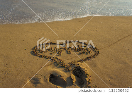 Messages of love written in the sand at sunset by the tranquil shoreline. 133250462