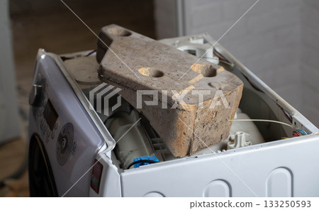 Unscrewed counterweight stone in a washing machine. The concept of noise and vibration when spinning a washing machine due to a defective counterweight, close-up Unscrewed counterweight stone in a washing machine. The concept of noise and vibration when spinning a washing machine due to a defective counterweight, close-up 133250593
