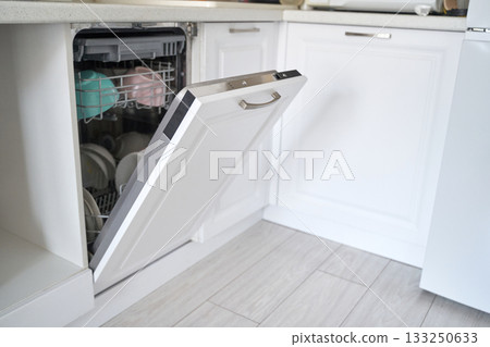 Modern white kitchen with open dishwasher revealing clean plates and cups 133250633