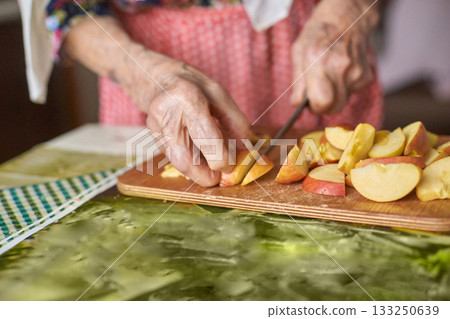 Elderly caucasian female slicing apples in kitchen with wooden cutting board 133250639