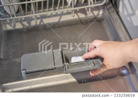 Hand placing dishwasher tablet in open dishwasher tray 133250659