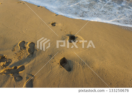 Footprints on a golden beach at sunset, where gentle waves caress the shore. Footprints on a golden beach at sunset, where gentle waves caress the shore. 133250676