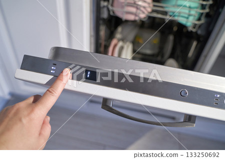 Caucasian female hand operating dishwasher control panel in kitchen setting Caucasian female hand operating dishwasher control panel in kitchen setting 133250692