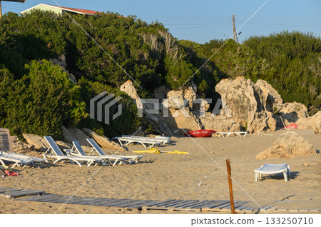Relaxing beachside view with loungers and rocky cliffs at sunset on a serene coastal afternoon. 133250710