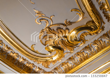 Close-up of an opulent gilded ceiling detail with ornate scroll work and gold leaf trims 133250847