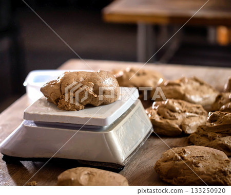 Dough portion placed on digital scale for precise measurement during food preparation process in bakery kitchen. Multiple dough pieces ready for baking. Dough portion placed on digital scale for precise measurement during food preparation process in bakery kitchen. Multiple dough pieces ready for baking. 133250920