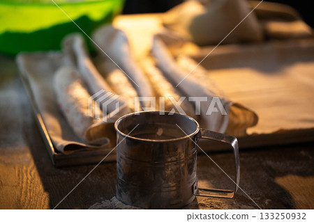 Flour sifter on wooden table, baking preparation, kitchen scene, dough rising in background, rustic domestic setting, culinary process, artisan bread making, traditional food craft 133250932