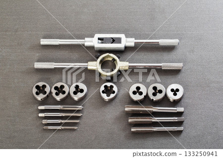 Precision metalworking tap and die set including tap wrenches and various thread cutting tools displayed on dark gray surface for mechanical engineering and repair projects 133250941