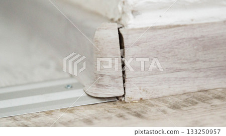Broken corner of plastic modern skirting board on gray floor, industrial, close-up 133250957