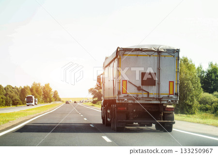 A truck pulls a grain semi-trailer with grain against the backdrop of the sun on a highway, industry. Copy space for text A truck pulls a grain semi-trailer with grain against the backdrop of the sun on a highway, industry. Copy space for text 133250967