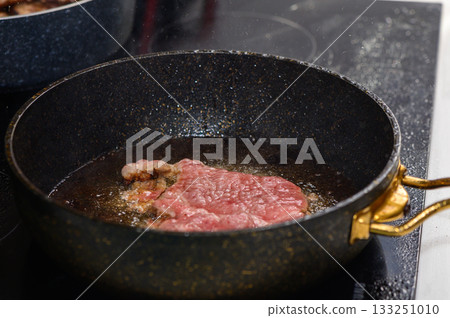 Sizzling steak cooking in a frying pan on a modern stovetop in a cozy kitchen setting Sizzling steak cooking in a frying pan on a modern stovetop in a cozy kitchen setting 133251010