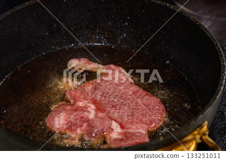 Cooking a juicy steak in hot oil in a skillet on the stove during a cozy evening at home Cooking a juicy steak in hot oil in a skillet on the stove during a cozy evening at home 133251011