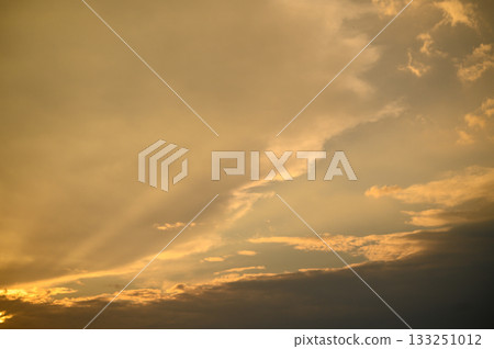 Golden rays break through soft clouds at sunset, creating a breathtaking sky over tranquil horizons 133251012