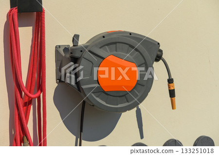 A bright orange retractable hose reel mounted on a garage wall on a sunny afternoon, ready for outdoor tasks 133251018