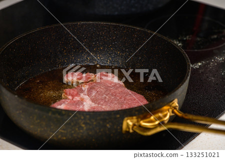 Sizzling steak cooking in hot oil on a stovetop skillet in a cozy kitchen during dinner preparation 133251021