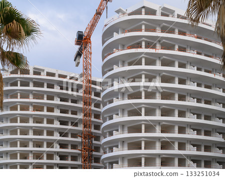 New modern building construction with curved architecture and crane under cloudy skies in an urban setting 133251034