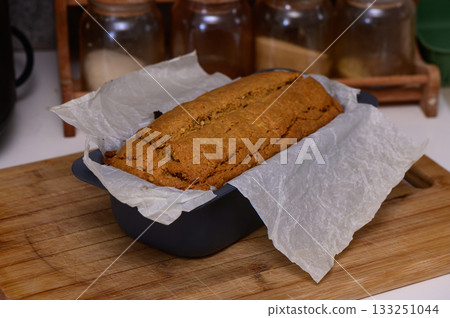 Freshly baked loaf of banana bread cooling on a wooden countertop with jars in the background Freshly baked loaf of banana bread cooling on a wooden countertop with jars in the background 133251044