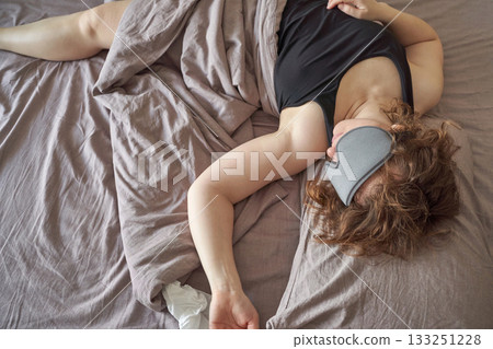 Caucasian young female sleeping peacefully in bed with eye mask and brown hair Caucasian young female sleeping peacefully in bed with eye mask and brown hair 133251228