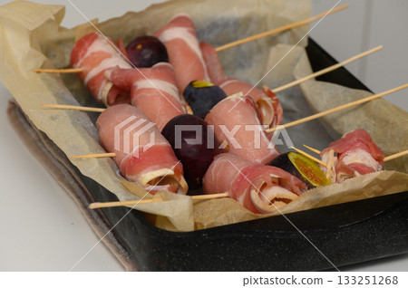 Delicious savory treats of wrapped meats and fruits prepared for a gathering or celebration 133251268