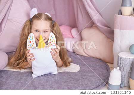 Smiling caucasian young girl in playful bedroom holding stuffed unicorn pillow Smiling caucasian young girl in playful bedroom holding stuffed unicorn pillow 133251340