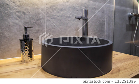 Stylish modern gray stone sink in the bathroom in a suspended wooden cabinet and a chrome tap. Gray tiles on the wall, interior Stylish modern gray stone sink in the bathroom in a suspended wooden cabinet and a chrome tap. Gray tiles on the wall, interior 133251389