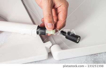Close-up of a man's hands replacing old, stuck microlifts in a white toilet seat and lid, close-up, industry 133251398