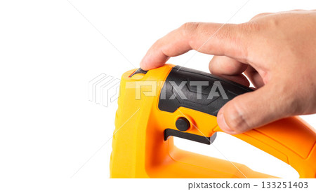 A yellow electric jigsaw in a worker's hand against a white background, isolated, close-up. Woodworking tool, industry A yellow electric jigsaw in a worker's hand against a white background, isolated, close-up. Woodworking tool, industry 133251403