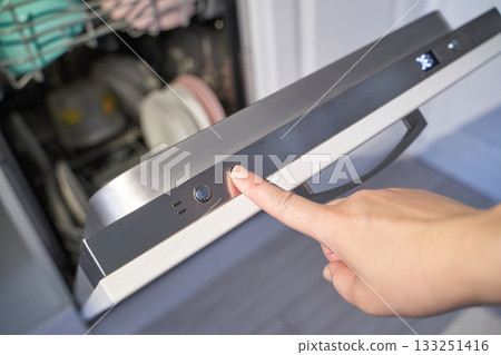 Female hand pressing start button on dishwasher door with clean dishes inside Female hand pressing start button on dishwasher door with clean dishes inside 133251416