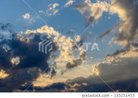Dramatic clouds swirling above serene landscape during golden hour light Dramatic clouds swirling above serene landscape during golden hour light 133251455