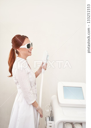 Female caucasian adult in white coat using laser hair removal device 133251553