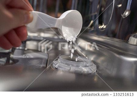 Hand pouring dishwasher salt into dispenser inside open dishwasher close up Hand pouring dishwasher salt into dispenser inside open dishwasher close up 133251613