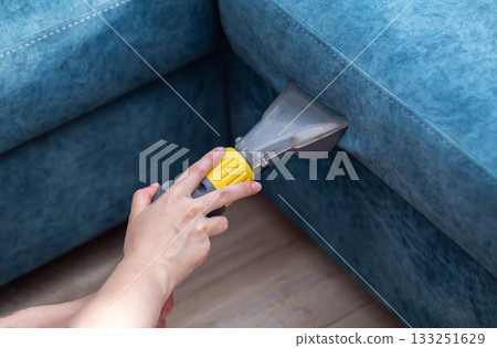 Person cleaning sofa upholstery with a specialized tool in a cozy living room setting during the day Person cleaning sofa upholstery with a specialized tool in a cozy living room setting during the day 133251629
