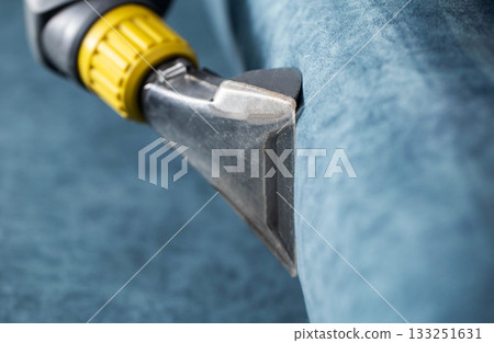 Cleaning process of a blue upholstered couch with a vacuum cleaner attachment in a cozy living room during daylight Cleaning process of a blue upholstered couch with a vacuum cleaner attachment in a cozy living room during daylight 133251631