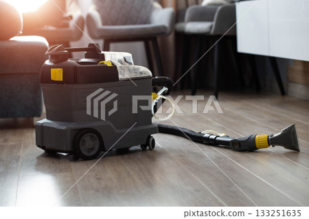 A modern upholstery vacuum cleaner stands in a room against a sunset backdrop. Cleaning service. Copy space for text, housework A modern upholstery vacuum cleaner stands in a room against a sunset backdrop. Cleaning service. Copy space for text, housework 133251635