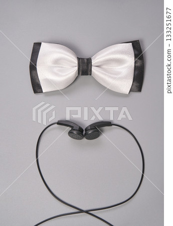 Elegant white bow tie and black earbuds on gray background for fashion and music Elegant white bow tie and black earbuds on gray background for fashion and music 133251677
