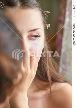Young caucasian female applying makeup in mirror with hair clips 133251699