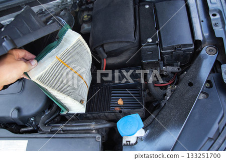 a mechanic's hand removes an air filter from the engine compartment of a car to replace it. Car maintenance, close-up a mechanic's hand removes an air filter from the engine compartment of a car to replace it. Car maintenance, close-up 133251700