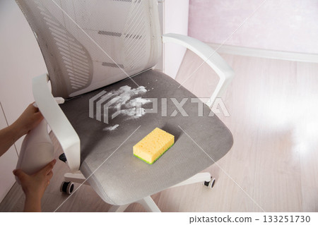 A woman's hand with a cleaning agent sprays a spray on the dirty upholstery of a computer chair. Concept of dry cleaning at home, industry 133251730