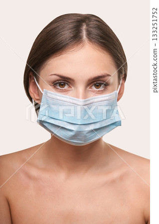 Young caucasian female with brown eyes wearing blue medical face mask on light 133251752