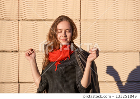 Caucasian young female in red scarf enjoying sunlight against textured wall Caucasian young female in red scarf enjoying sunlight against textured wall 133251849