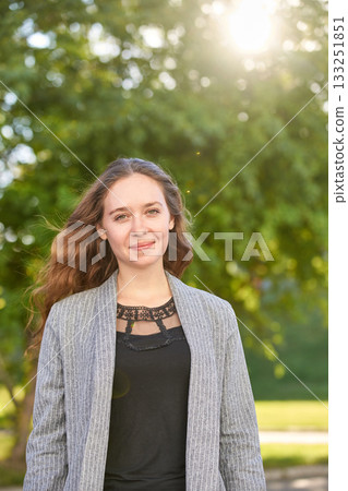 Young caucasian adult female smiling outdoors in sunlight with green trees Young caucasian adult female smiling outdoors in sunlight with green trees 133251851