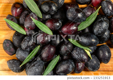 Freshly harvested black olives resting on a wooden surface with green leaves enhancing their rich color Freshly harvested black olives resting on a wooden surface with green leaves enhancing their rich color 133251913