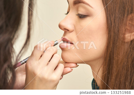 Close-up of young caucasian female undergoing makeup application with lip liner Close-up of young caucasian female undergoing makeup application with lip liner 133251988