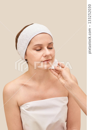 Caucasian female adult skincare routine with cotton pad and headband on neutral 133252030